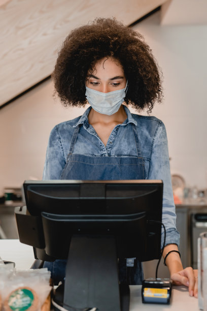 非洲年轻女服务员在咖啡馆收银台戴着医用口罩工作竖版照片图片下载