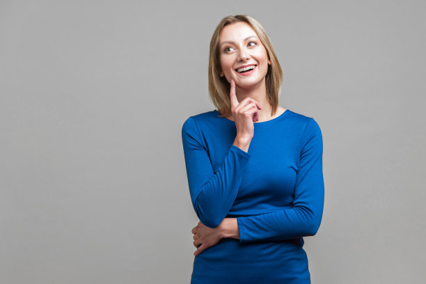 肖像可爱的积极的女人在蓝色裙子指向手指向上和触摸脸，有一个伟大的想法。在灰色背景上隔离图片下载