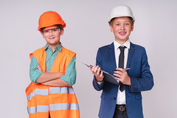 两个小男孩未来的工程师和建筑工人戴着安全帽在灰色的背景下孤立图片下载