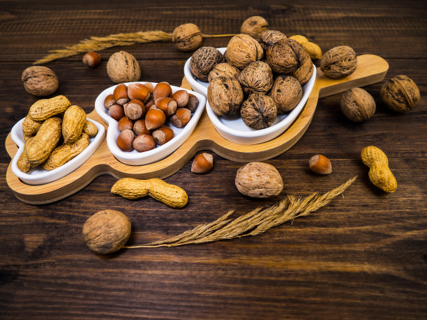 胡桃、榛子和花生放在一个白色的心形盘子里，木头做的背景。食物。图片下载