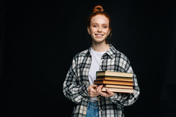 开朗的年轻女大学生拿着书，看着孤立的背景上的相机。图片下载