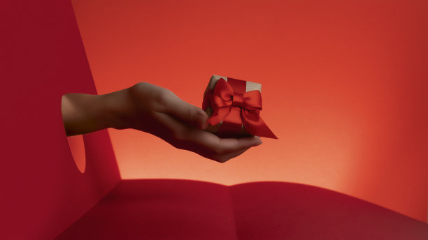 手握礼品盒装饰红丝带和牛皮纸在红色背景剪纸圈。圣诞假期，除夕。交付的礼物。销售横幅，文字空间。图片下载