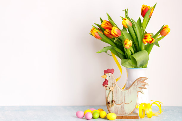 白色的罐子里放着一束新鲜的黄色郁金香，背景是白色的复活节彩蛋。图片下载
