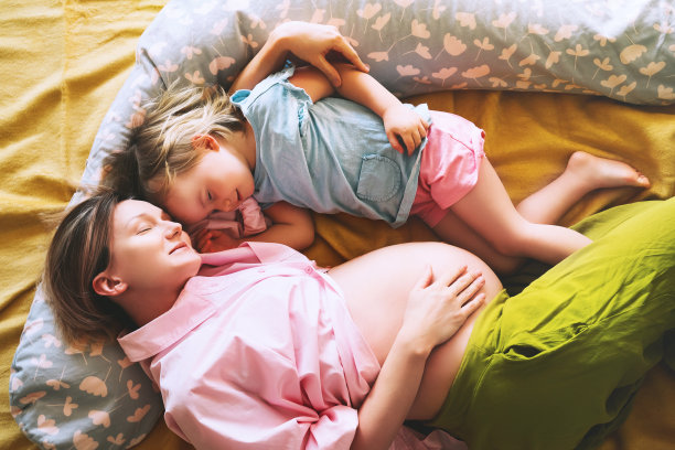 怀孕的母亲和女儿一起在家。第二次怀孕时带着第一个孩子的妇女。母亲和育儿理念。幼童微笑的女孩和妈妈。图片下载