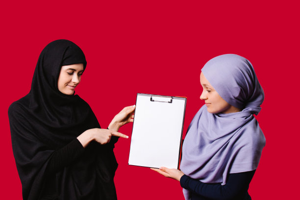 穆斯林女学生戴着头巾，用食指拿着一张白纸。教育理念与空白的广告空间。图片下载