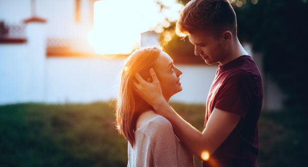 白人男子拥抱他的女人看着她的眼睛，微笑着摆出日落的背景图片下载
