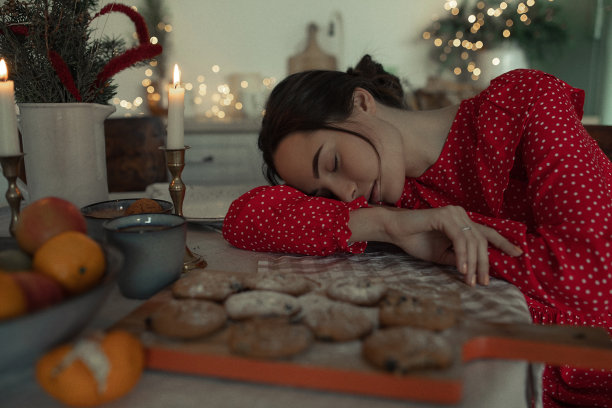 疲惫的女人睡在厨房桌子旁边，背景是圣诞装饰。图片下载