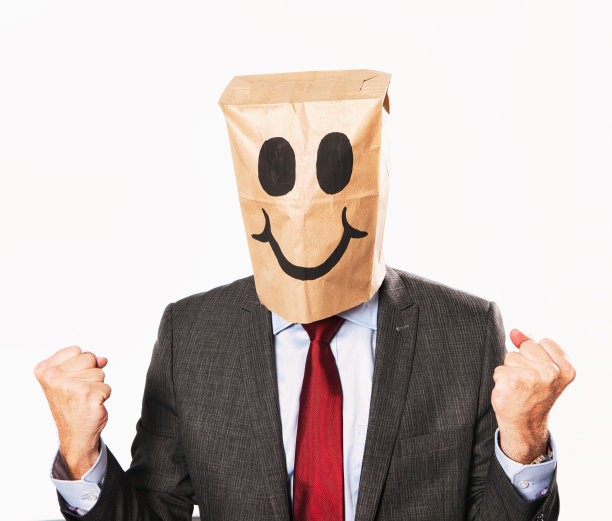 西装革面的快乐商人，戴着卡通纸袋，得意地握紧拳头图片下载