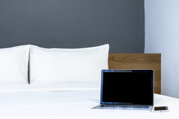 笔记本电脑与空白屏幕与智能手机在白色的床上装饰在酒店卧室的室内背景，工作和商务在休闲与旅游在假日的概念。图片下载