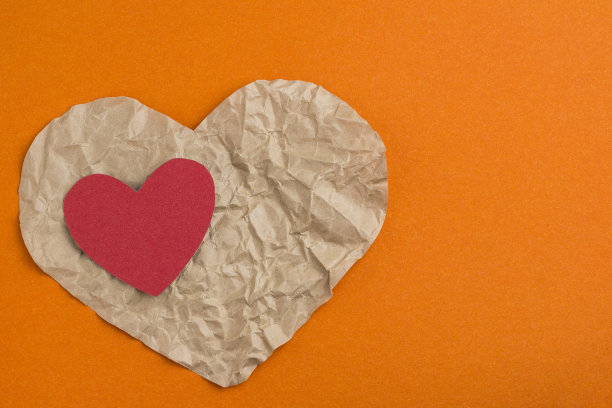 橘色背景上的纸心。情人节。皱巴巴的心。图片下载