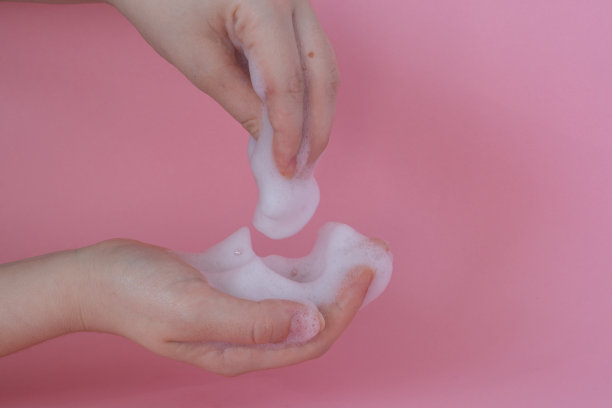 特写女人的手与脸泡沫，手泡沫在粉红色的背景图片下载