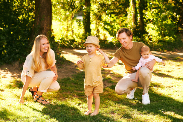 户外肖像快乐的家庭在夏季公园的乐趣，年轻夫妇与蹒跚学步的男孩和女婴图片下载