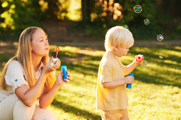 快乐的年轻妈妈和可爱的蹒跚学步的男孩在夏日公园玩肥皂泡，快乐的童年图片下载