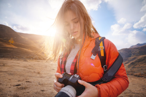 年轻的潮女人手里拿着相机在背光山里。头发在风中飘扬图片下载