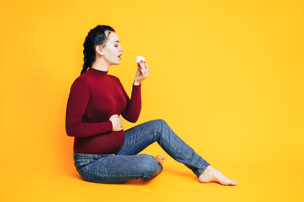 黄色背景下穿着红色毛衣和蓝色牛仔裤的孕妇。关心孕妇的健康图片下载