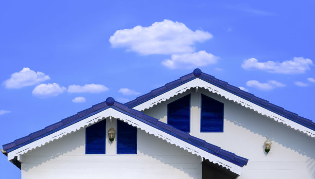 蓝色纤维水泥瓦屋顶不同层次，滴漏屋檐在白色木屋上，映衬着白云蓝天图片下载