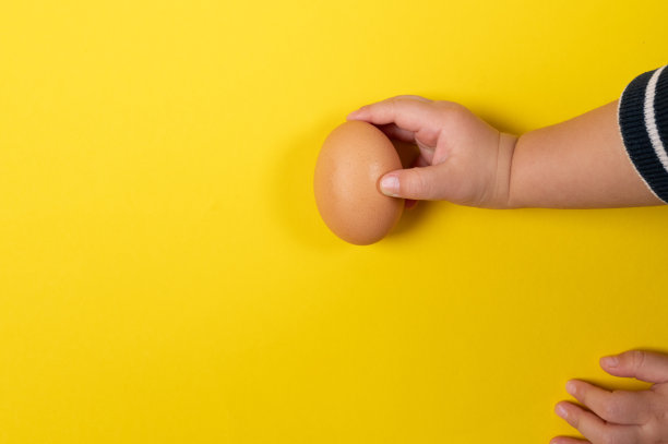 孩子手里拿着黄色背景上的棕色鸡蛋。健康食品与有机食品理念图片下载