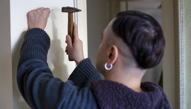 年轻人在白墙上钉钉子图片下载