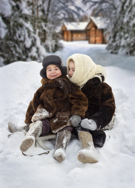 两个穿着暖和的毛皮大衣的孩子坐在雪地里，以森林为背景图片下载