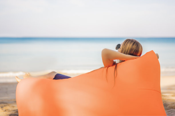 夏天的生活方式肖像漂亮的女孩坐在橙色充气沙发上的热带岛屿的海滩。在气垫床上轻松享受生活图片下载