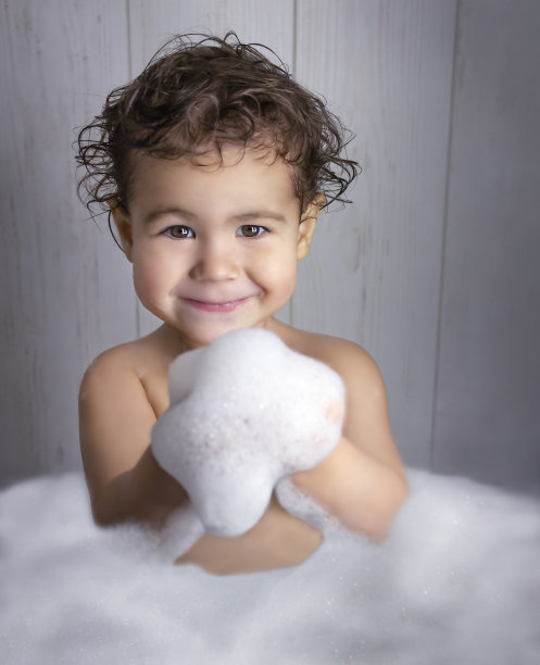 在泡泡浴中的婴儿手里拿着泡沫，看着镜头图片下载