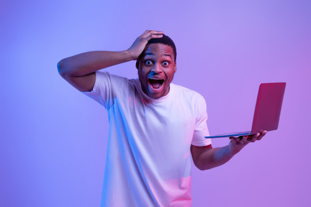 在线赢。震惊的黑人拿着笔记本电脑，兴奋地摸着头图片下载