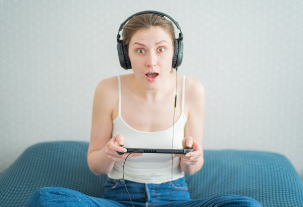 比赛赢了。快乐的女玩家戴着耳机为游戏中的胜利而欢呼。情感的玩家。便携式游戏机图片下载