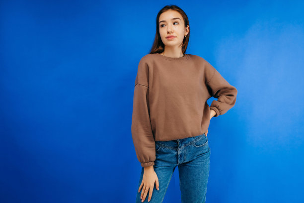 穿着帽衫的年轻女子在工作室蓝色背景下摆姿势图片下载