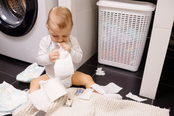 婴儿或蹒跚学步的婴儿撕卫生纸并吃掉它。地板上有许多卷。特写镜头图片下载