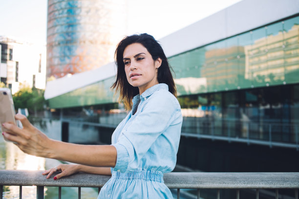 严肃的黑发白人女性千禧摆姿势自拍在城市设置在空闲时间在市中心使用手机美丽的女性博主制作照片或在智能手机上的社交网络图片下载