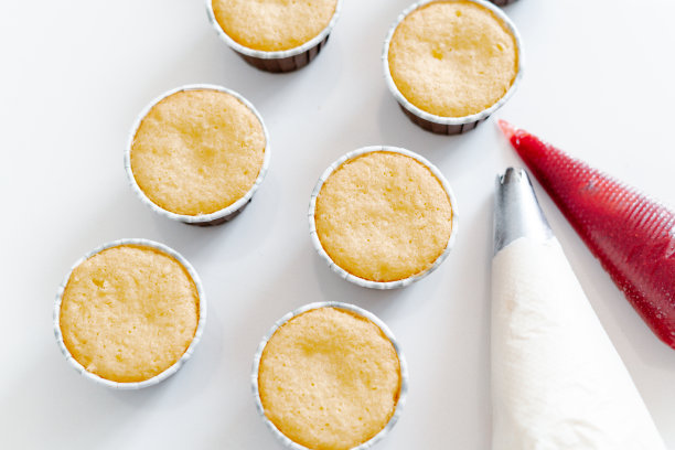 新鲜出炉的纸杯蛋糕放在一张白色的桌子上，旁边是用红草莓和白色奶油芝士填充的烹饪套筒。早餐食品。新鲜烘焙的纸杯蛋糕当甜点。图片下载