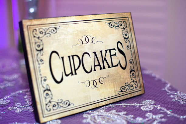 紫色桌布上的黑色字母和华丽设计的“纸杯蛋糕”标志图片下载