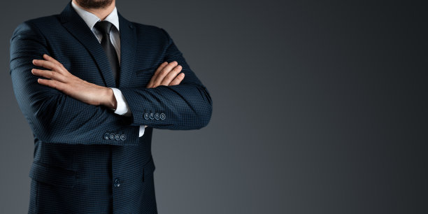 一个穿着西装的男人双手交叉站在灰色的背景上。概念商，商务沟通。特写镜头。图片下载