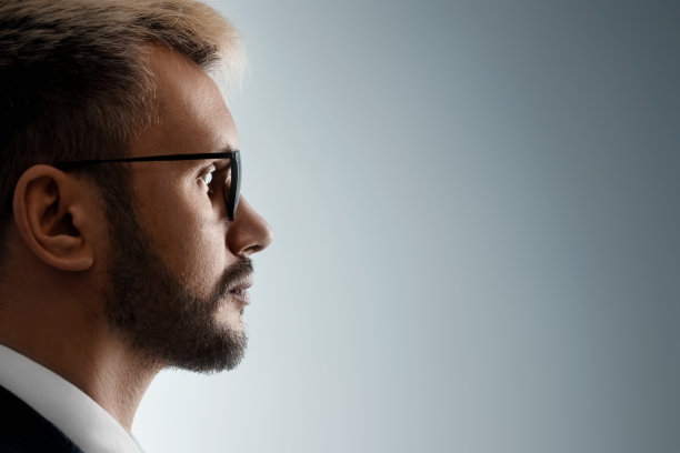 一个男人的特写肖像与眼镜在侧面看从黑暗的光。面部表情中性，复制空间。图片下载