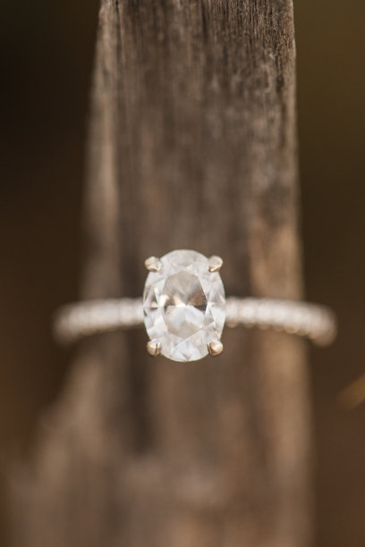 椭圆形钻石白金订婚戒指的微距照片在棕色的木头上在海滩上图片下载