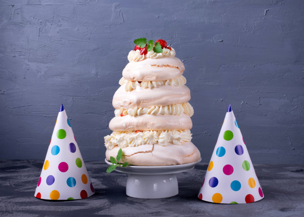 高的巴芙洛娃蛋糕，奶油，草莓和生日帽子图片下载