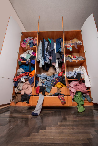 巨大的衣橱里堆满了旧衣服，胡乱地从架子和衣架上往下推挂着。衣柜混乱图片下载