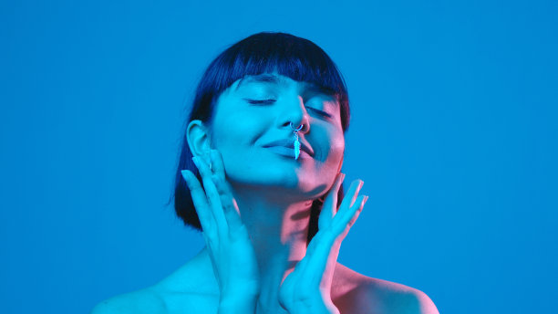 年轻女子触摸她的脸孤立在蓝色霓虹灯copyspace图片下载