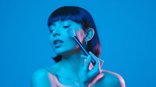 年轻女子用化妆刷隔离在蓝色霓虹copyspace图片下载