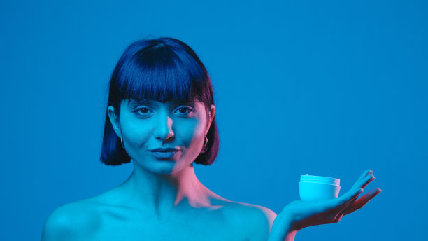 年轻女子涂抹面霜孤立在蓝色霓虹copyspace图片下载