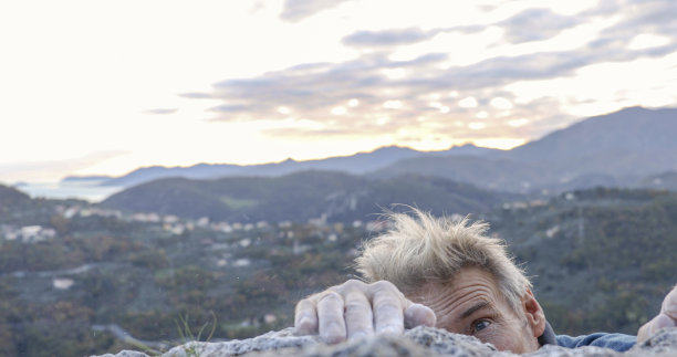 男性攀岩者用涂了粉笔的手伸向岩石顶峰图片下载