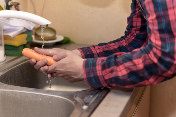 一个不认识的男人在厨房水槽里洗胡萝卜的照片。图片下载