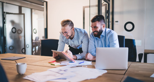 成功的年轻男同事在为合作项目做研究时友好的交谈，快乐的商人在办公室大笑，在工作过程中玩得很开心图片下载