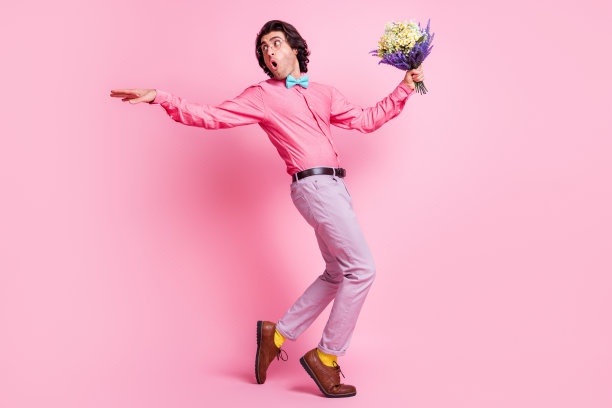 全尺寸的个人资料侧面照片funky棕色头发的男人回头看，手持鲜花，戴蓝色领结去孤立在粉红色的背景图片下载