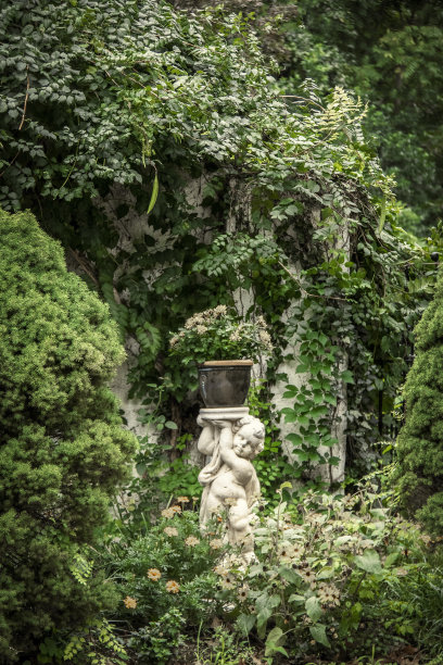 丘比特植物抱着盆花站在花园凹室藤蔓和更多的花靠近乡村墙。图片下载