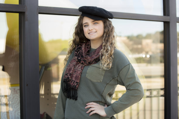 可爱的年轻女子戴着时髦的贝雷帽站在一家商店的橱窗前。她自信地看着镜头。图片下载