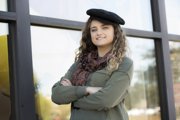 可爱的年轻女子戴着时髦的贝雷帽站在一家商店的橱窗前。她自信地看着镜头。图片下载