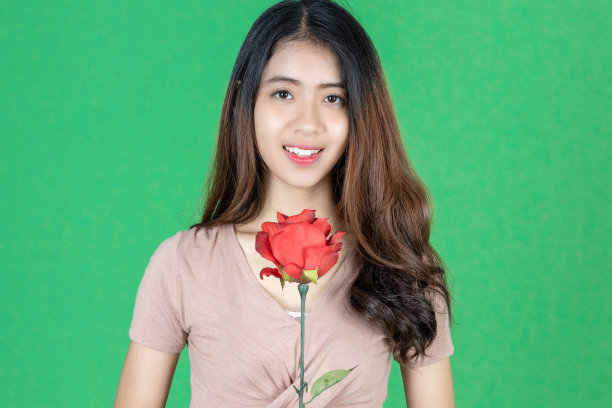 迷人的年轻亚洲女人在绿色孤立的背景上举着玫瑰。爱和情人节图片下载