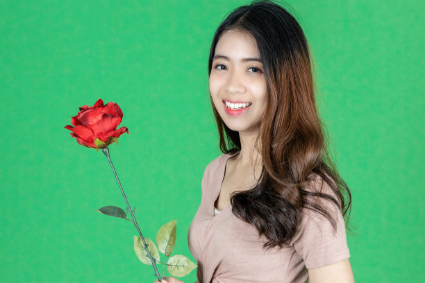 情人节的爱情和浪漫。美丽年轻的亚洲女人举着玫瑰在绿色孤立的背景。图片下载