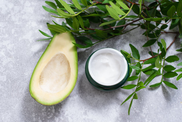 奶油酪梨籽提取物。保湿霜，为皮肤的背景鳄梨和树叶图片下载